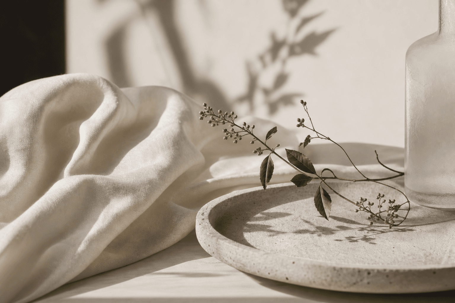 Botanical stems on ivory linen and a pale stone tray.